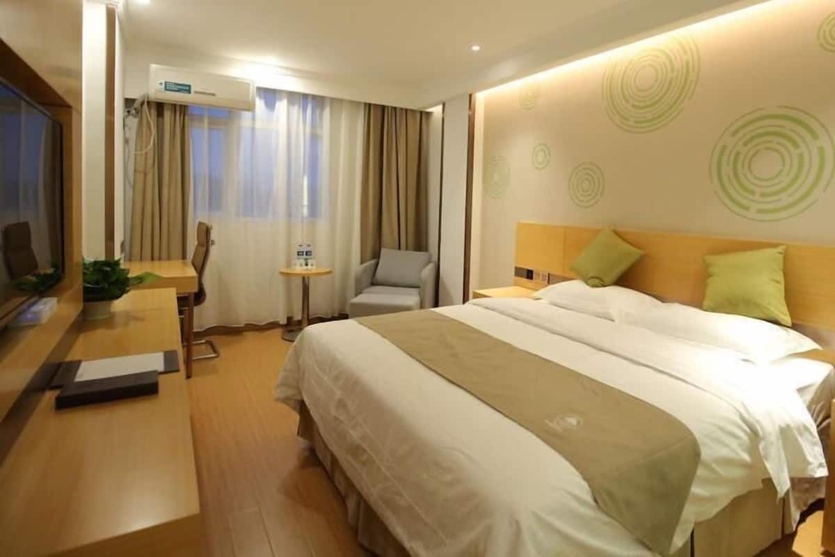 Una habitación de hotel con una cama, un escritorio, una silla, una mesita y un equipo de aire acondicionado.