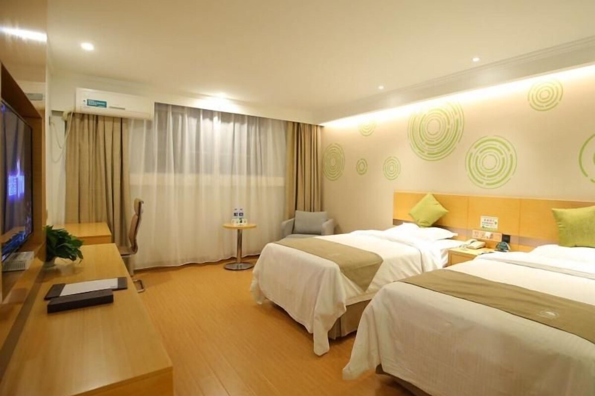 A hotel room with two beds, a desk, a TV, and a small table with a plant.