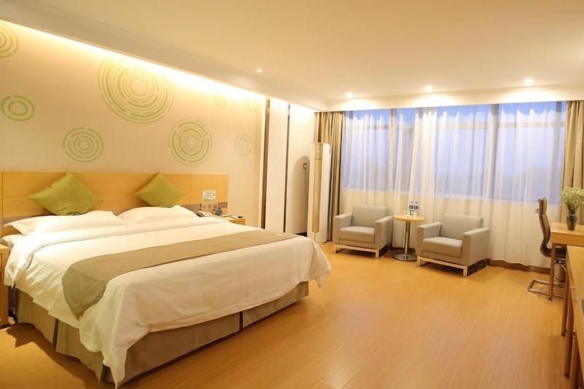 Quarto de hotel com uma cama grande, duas poltronas, uma mesa pequena e uma escrivaninha.