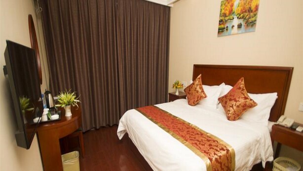 Une chambre d’hôtel comprenant un lit, un bureau avec un téléphone, une télévision et une fenêtre avec des rideaux.