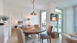 Een moderne eetruimte met een ronde houten tafel, witte stoelen en een hangende hanglamp.