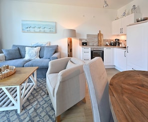 A modern kitchen with white cabinets, a wooden countertop, and a coffee maker. There is a dining area with a wooden table and chairs.