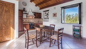 Une cuisine avec des meubles en bois, une table à manger et des chaises. Il y a une fenêtre donnant sur un paysage verdoyant.