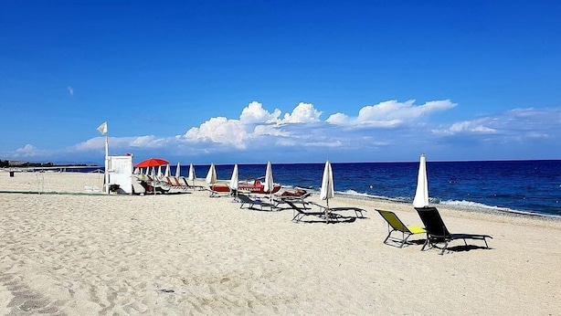 Une plage bordée de rangées de chaises longues et de parasols, avec une tour de surveillance et l’océan en toile de fond.