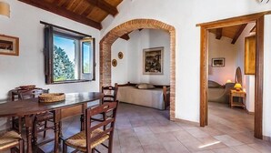 Un coin repas avec une table et des chaises en bois, une fenêtre donnant sur la forêt et un espace salon confortable avec un lit et une lampe.