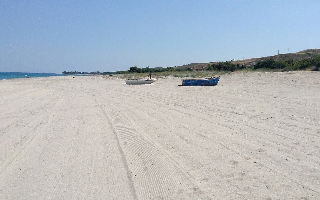 Een zandstrand met twee boten, één wit en één blauw, en een heldere lucht.