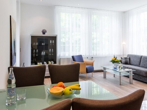 A modern living room with a glass dining table, brown chairs, a sofa, and a glass coffee table.