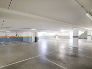 A spacious indoor parking area with clear ceiling lights, marked parking spaces, and a central pillar.