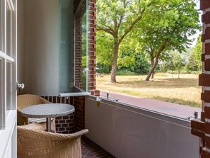 A balcony with wicker furniture and a view of a grassy area with trees.