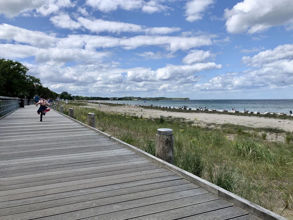 Een houten looppad dat naar een strand leidt, met een heldere lucht en land in de verte.