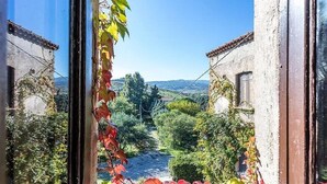 Une ruelle étroite aux murs de pierre, bordée de verdure, qui mène à un point de vue lointain sur des collines.