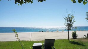 En strandutsikt med två solstolar som vetter mot havet, en klar himmel och en avlägsen kustlinje med båtar.