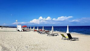 Une plage bordée de rangées de chaises longues et de parasols, avec une tour de surveillance et l’océan en toile de fond.
