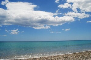 Ein Strand mit klarem türkisblauem Wasser und Kiesstrand, blauem Himmel mit vereinzelten Wolken.