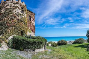 Ein aus Stein gebautes Gebäude mit Efeu bewachsenen Mauern, einer Rasenfläche und Blick auf das Meer.