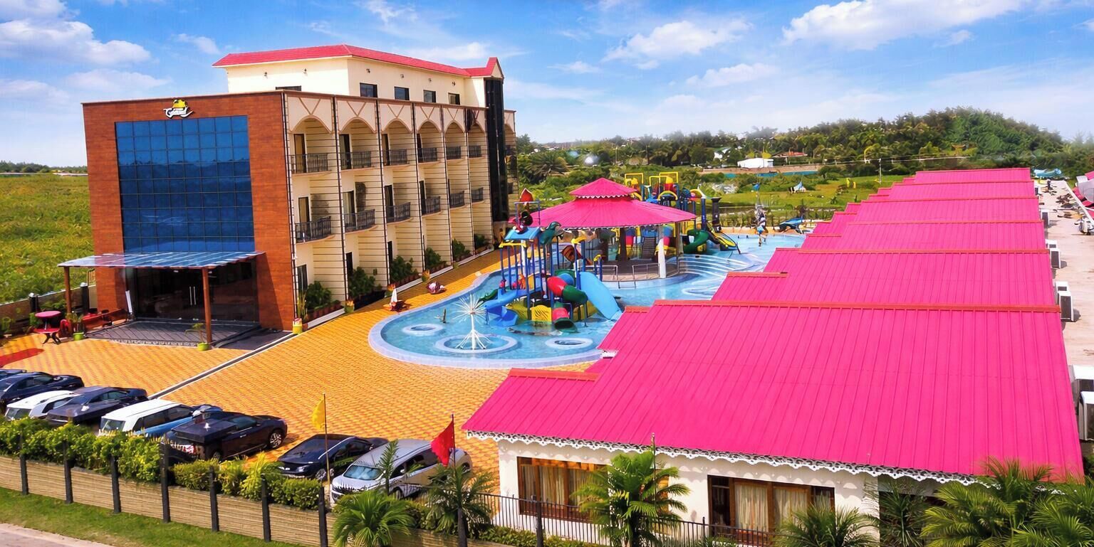 A hotel with a large parking lot, a playground, and a building with a red roof.