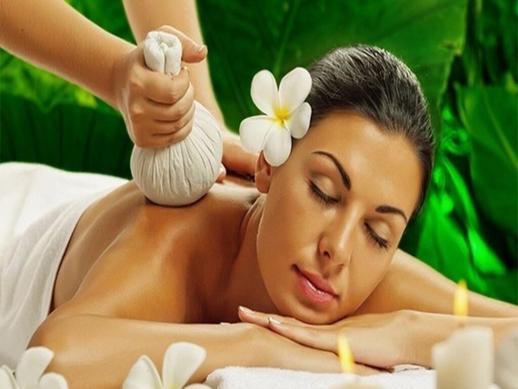 A person receiving a massage with a flower in their hair, lying on a massage table with a green background.
