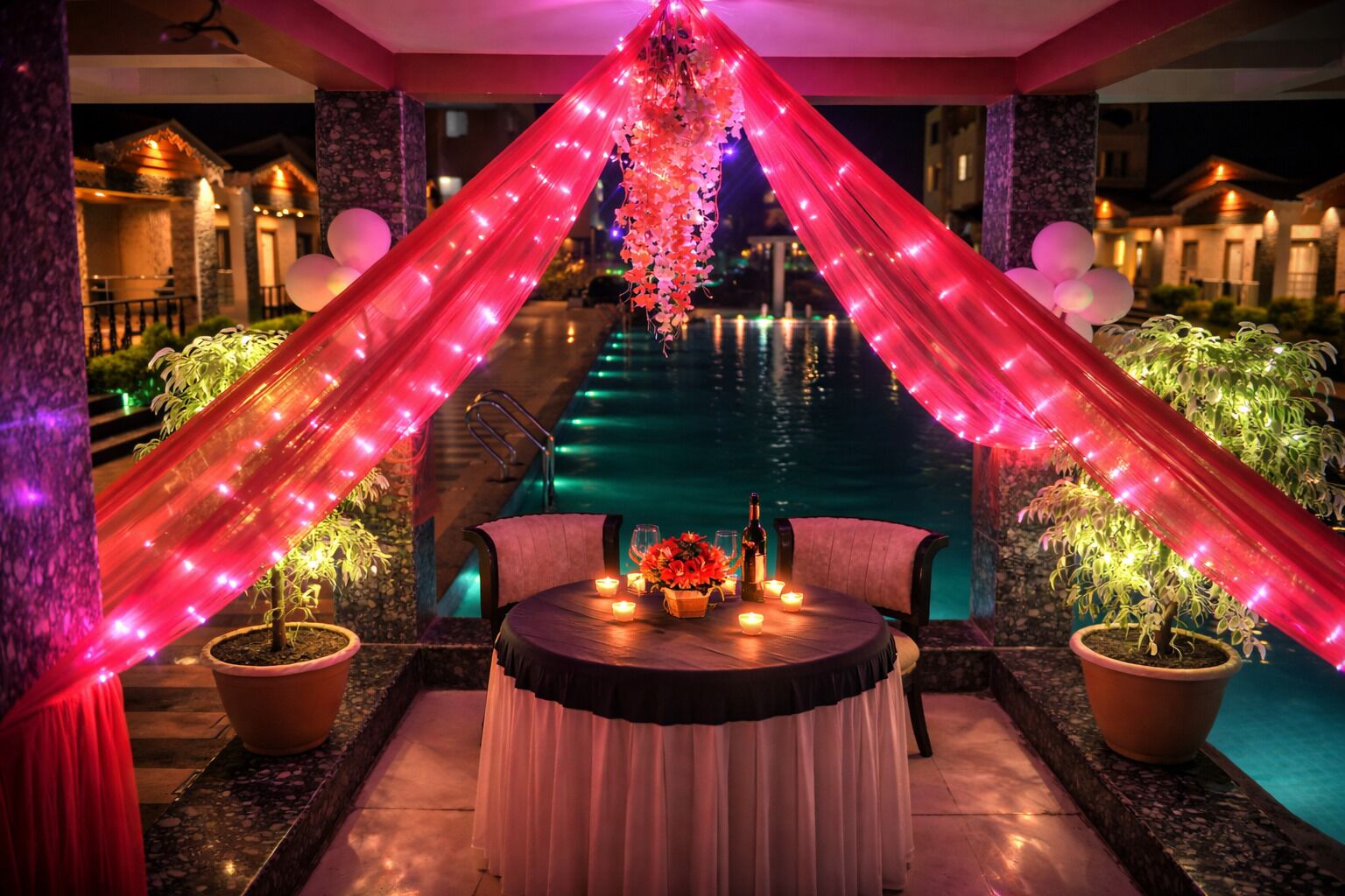 A romantic outdoor setting with a pool, draped lights, and a table with candles.