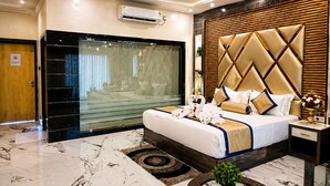 Una habitación de hotel moderna con una cama grande, un separador de vidrio, un cabecero de madera y un suelo de mármol.