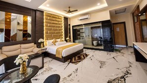 Una habitación de hotel moderna con una cama grande, un sofá, cabina de ducha con paredes de vidrio y un área de comedor.