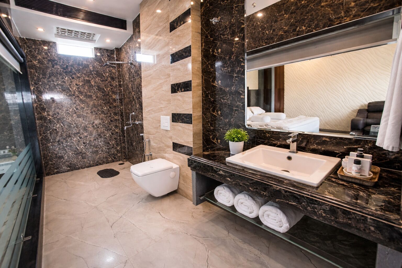 A modern bathroom with a marble vanity, a large mirror, a toilet, and a shower area.