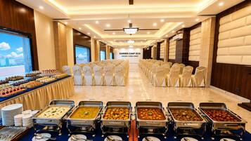 A banquet hall with rows of chairs, buffet with various dishes, and a large screen displaying 'Summer Camp 2026 Explore | Learn | Grow'.