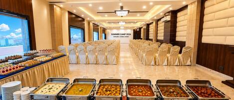 A banquet hall with rows of chairs, buffet with various dishes, and a large screen displaying 'Summer Camp 2026 Explore | Learn | Grow'.