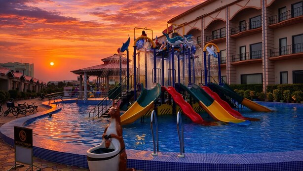 Zona de piscina con varias toboganes y un atardecer de fondo.