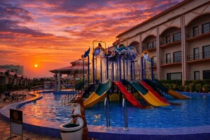 Zona de piscina con varias toboganes y un atardecer de fondo.