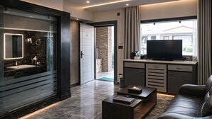 Una sala moderna con sofá, mesa de centro, televisor, y un baño con espejo y lavamanos.