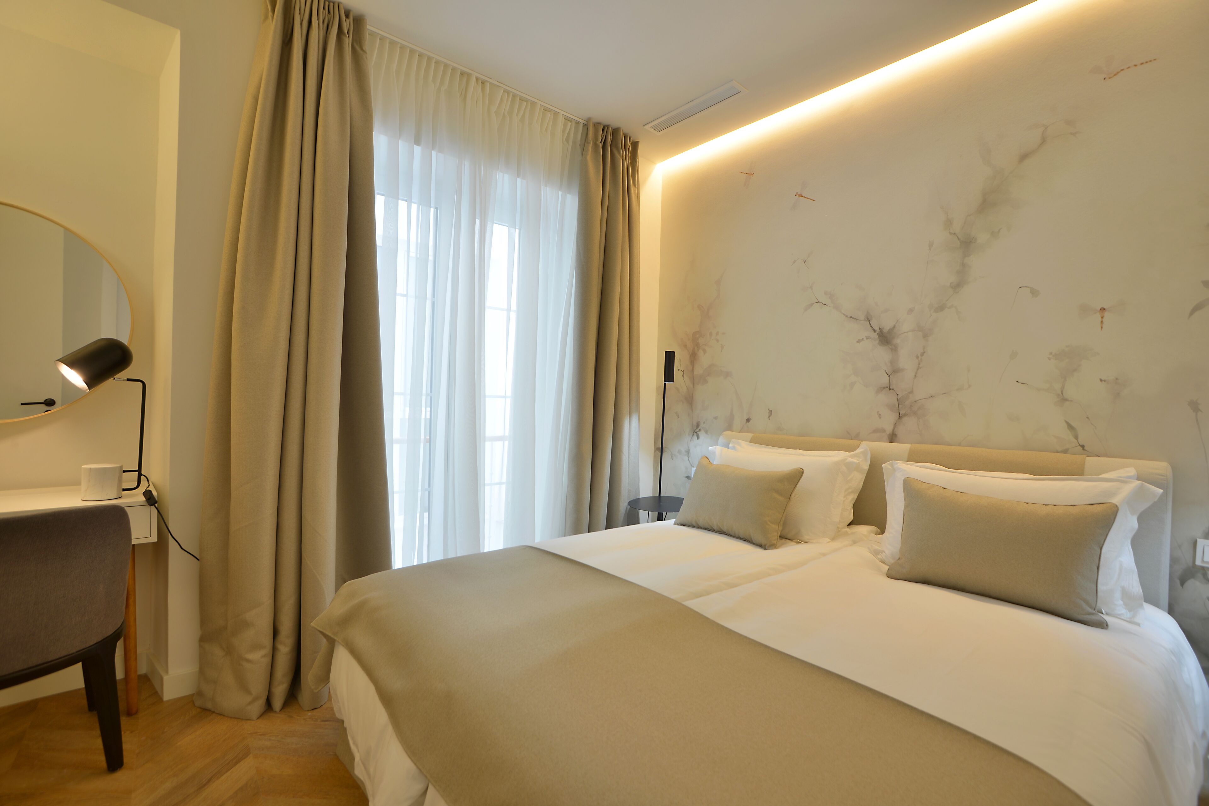 Quarto de hotel com cama, escrivaninha, luminária e parede com design semelhante a mármore.