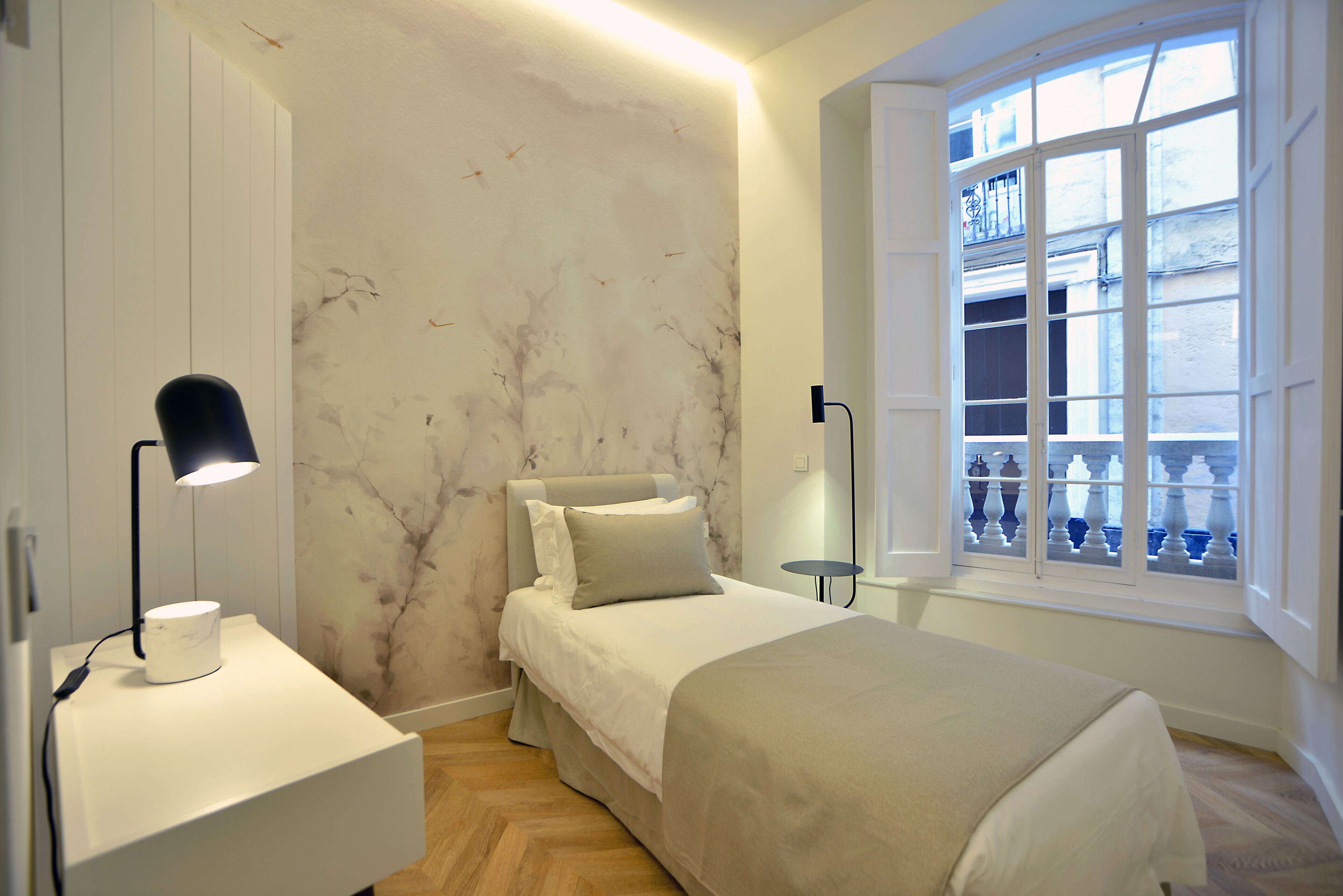 A bedroom with a bed, bedside tables, a nightstand, a window with a view, and a wall with a marble-like pattern.