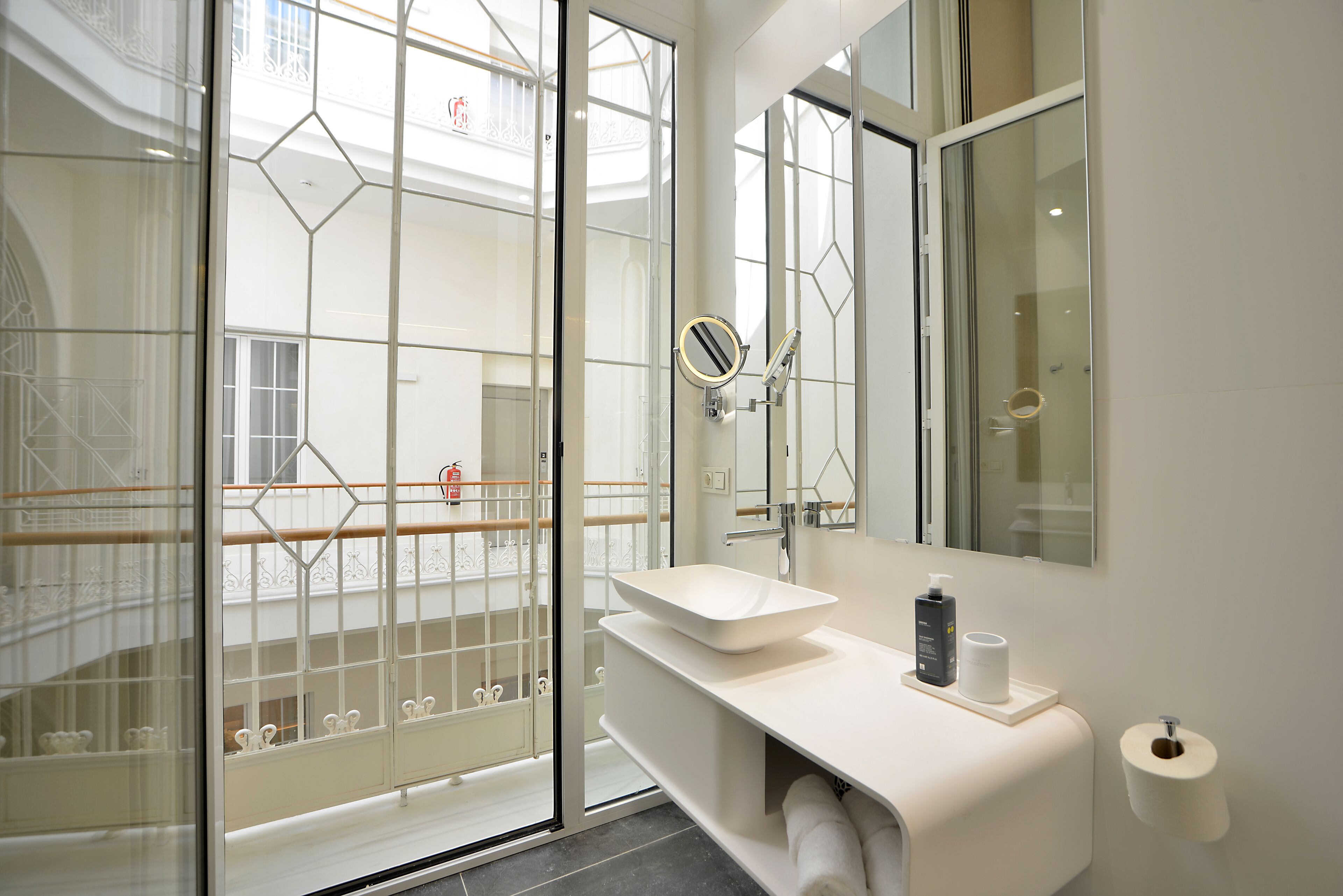 Casa de banho moderna com porta de vidro para uma varanda, um espelho grande e lavatório branco com artigos de higiene pessoal.