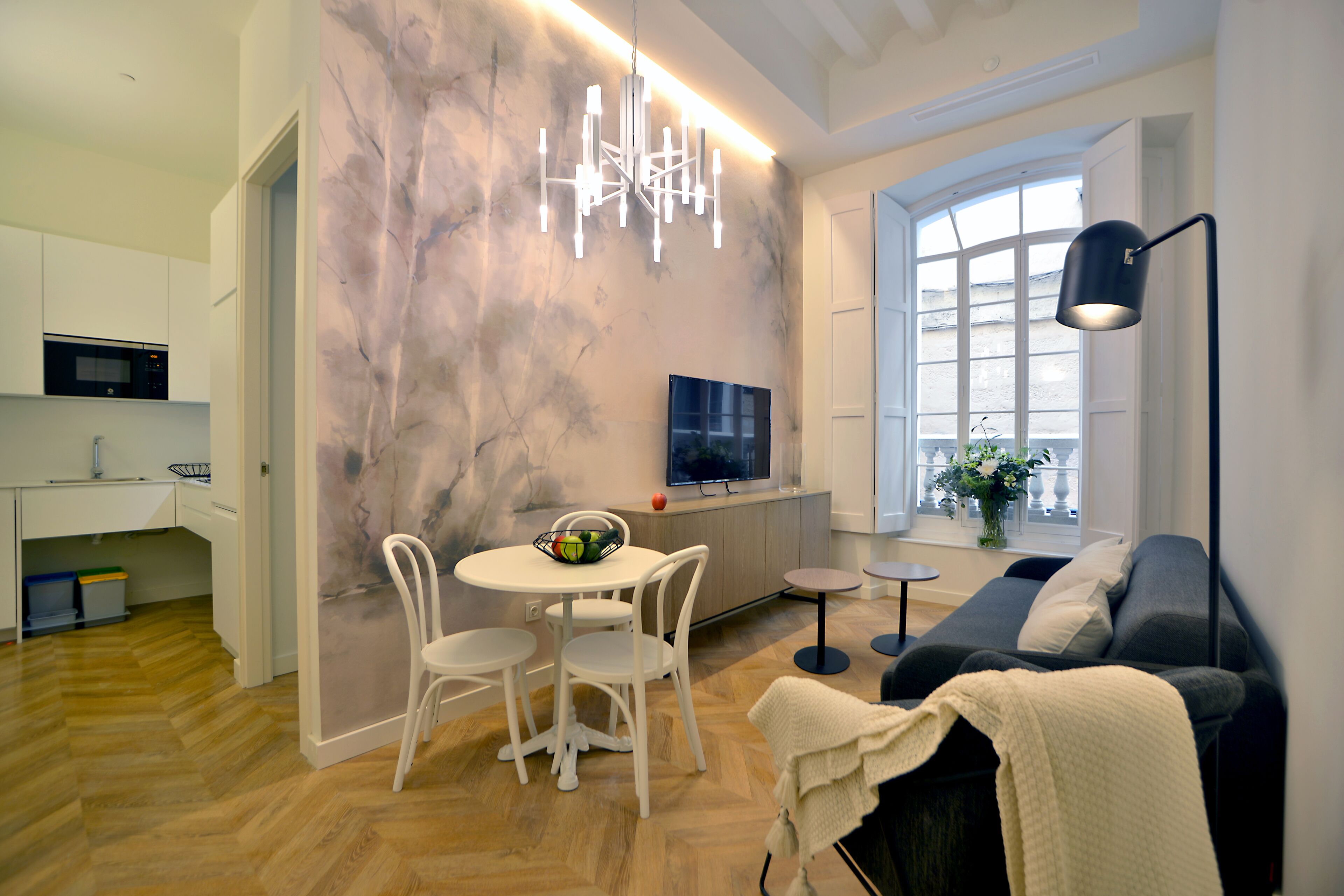 Una sala de estar moderna con sofá, televisor, mesa de comedor con sillas y una zona de cocina con microondas.