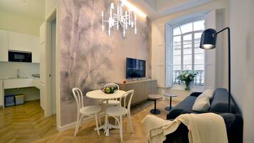 Una sala de estar moderna con sofá, televisor, mesa de comedor con sillas y una zona de cocina con microondas.