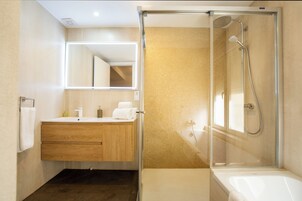 A modern bathroom with a glass shower enclosure, a standalone bathtub, and a vanity with a mirror and towel rack.