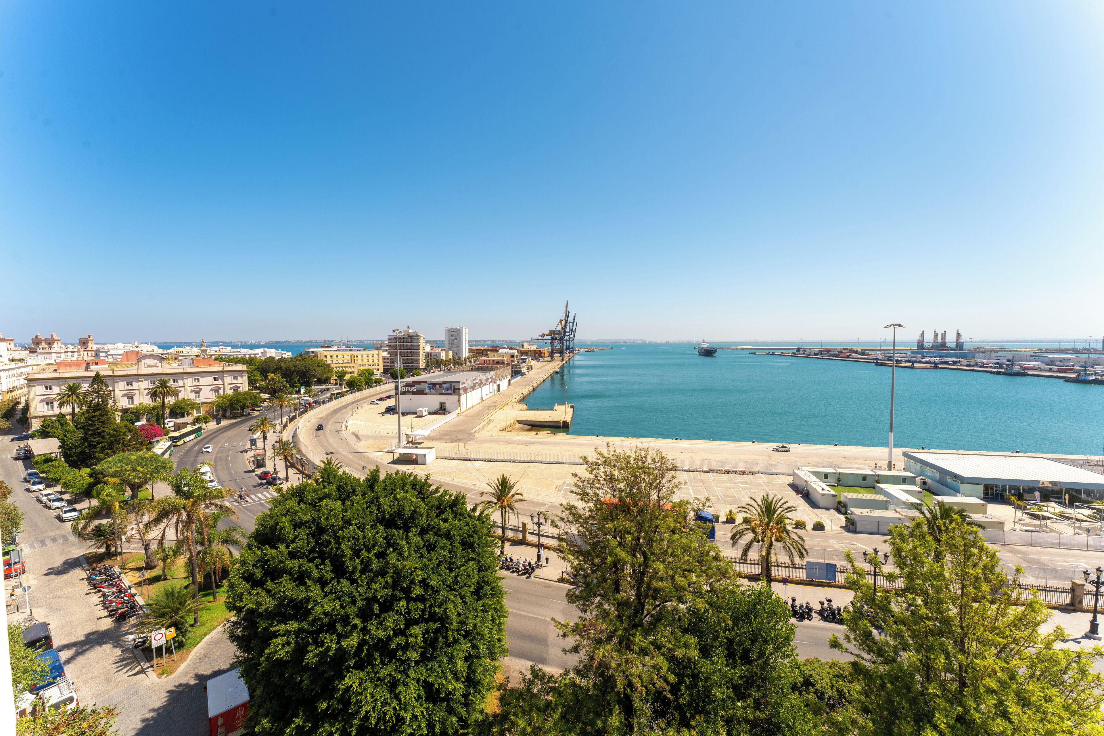 Paisagem costeira com um porto, edifícios e uma estrada serpenteando à beira-mar.