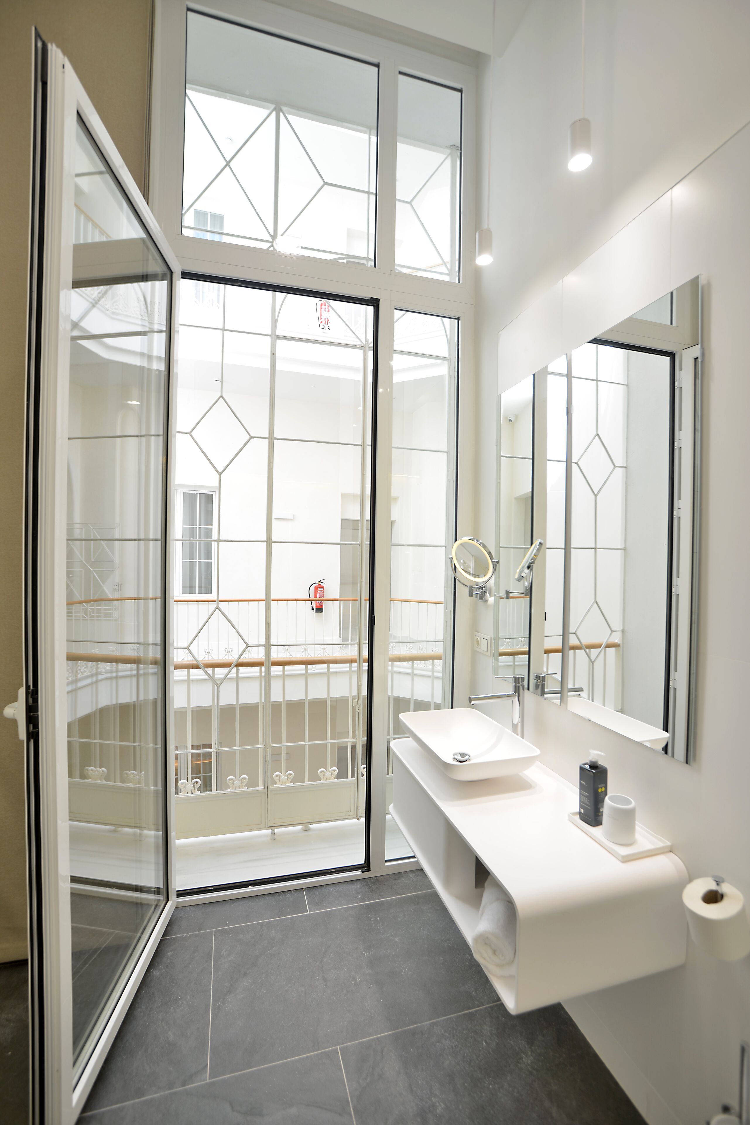 A modern bathroom with a glass door leading to a balcony, a white sink, a large mirror, and a towel rack.