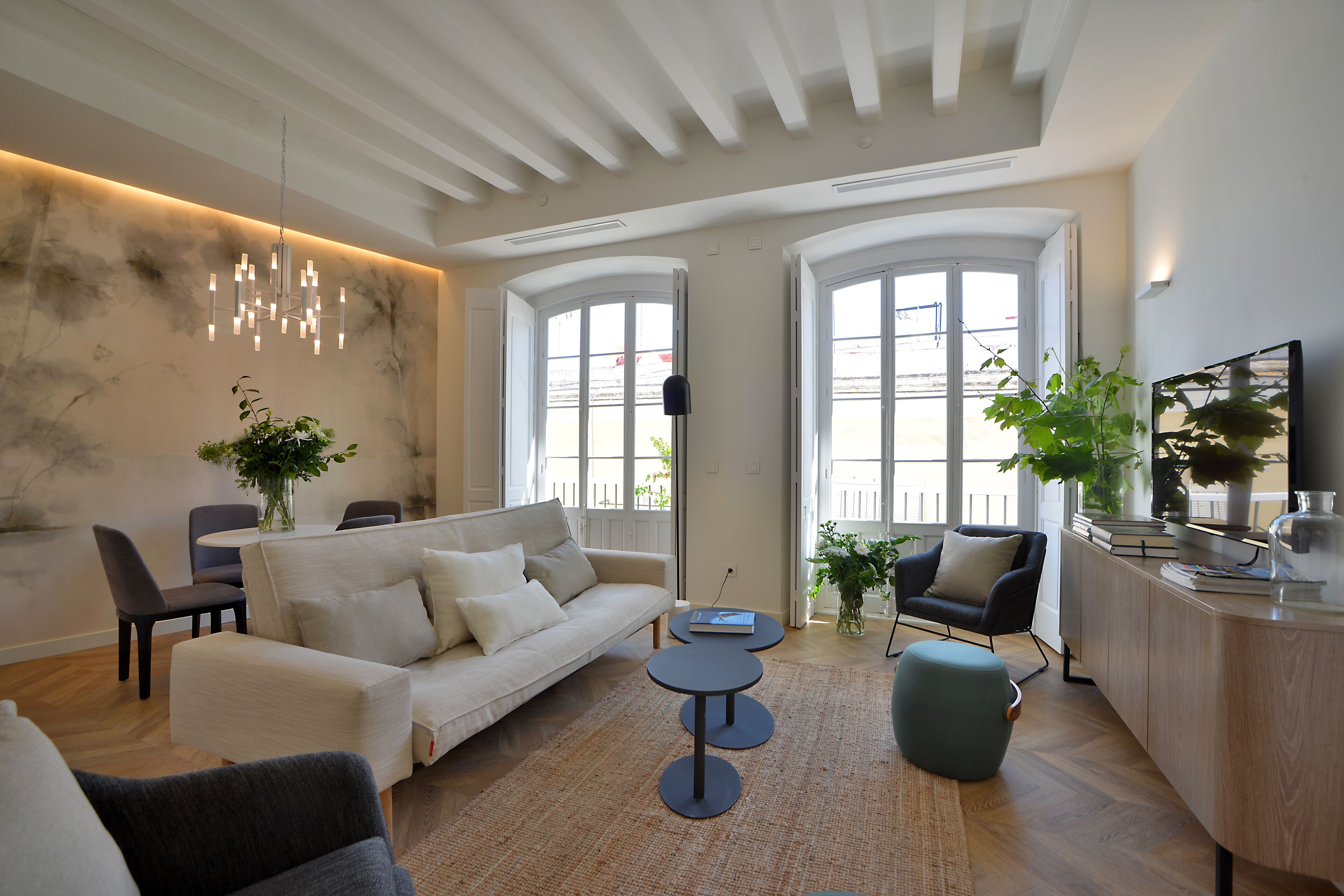 Un salon moderne avec un canapé, deux tables rondes et une table basse. On y trouve également des chaises, une bibliothèque et un téléviseur posé sur un meuble en bois.