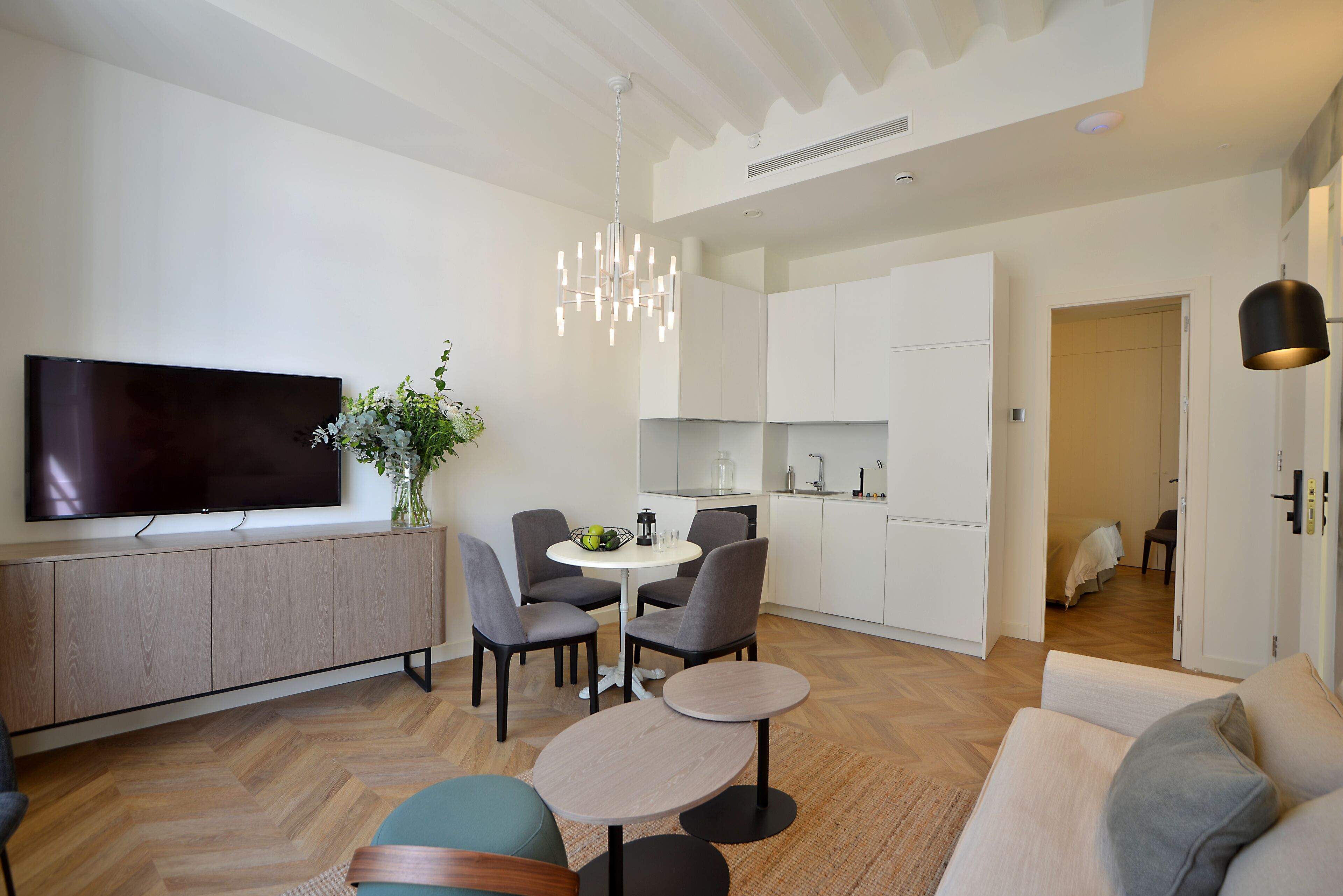 Una sala de estar moderna con un televisor de pantalla plana, una mesa de comedor con sillas, un sofá y una pequeña mesa de centro.