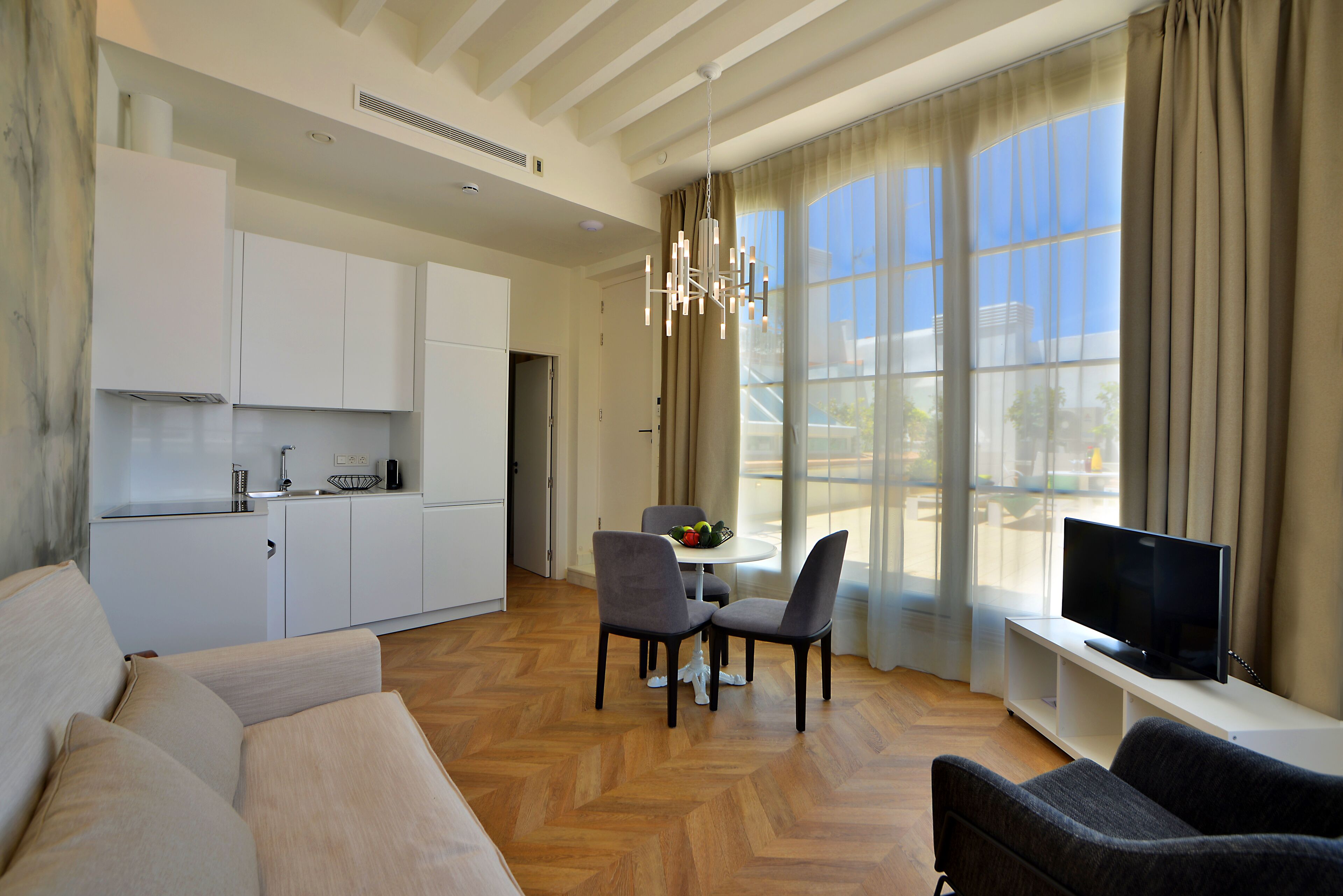 A modern living room with a sofa, two chairs, a TV, and a dining table with a fruit bowl.