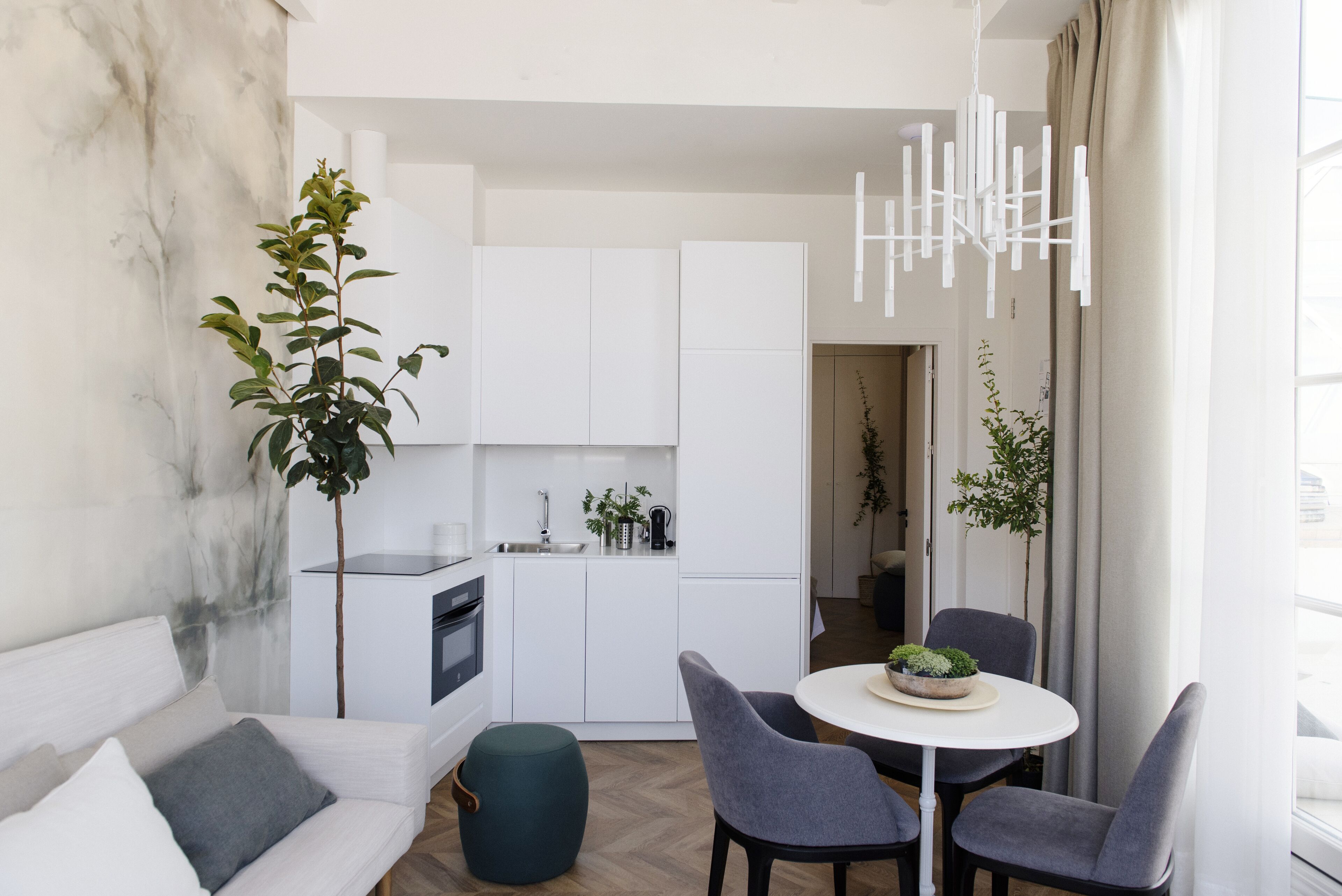 A modern kitchen with white cabinets, a built-in oven, and a dining area with a round table and two chairs.
