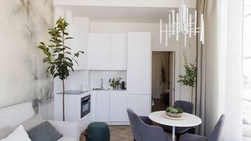 A modern kitchen with white cabinets, a built-in oven, and a dining area with a round table and two chairs.