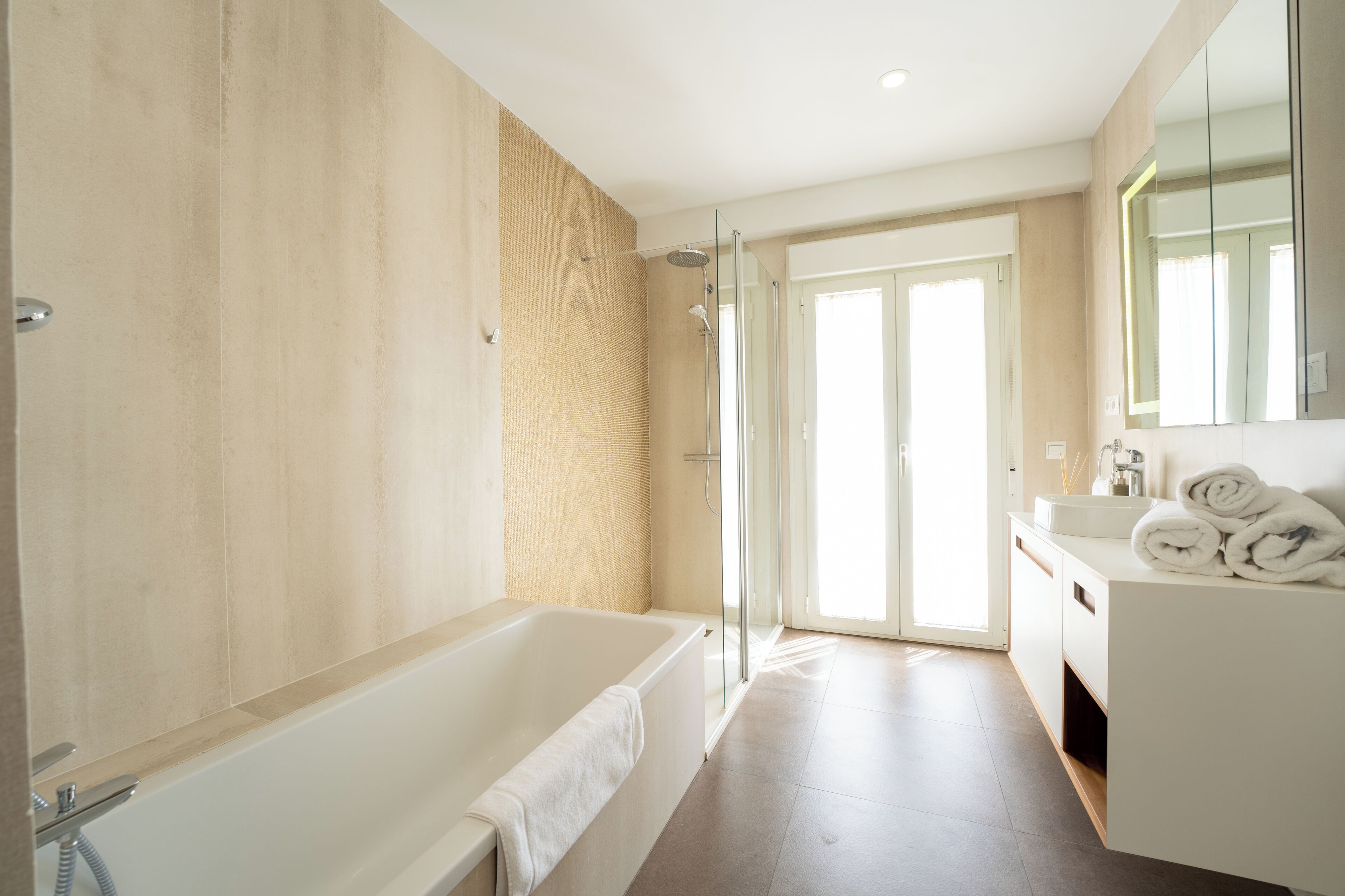 A modern bathroom with a bathtub, shower, and a vanity with towels.