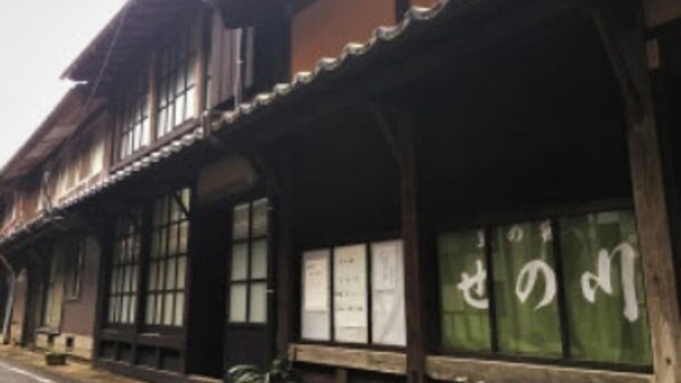 Un edificio tradicional de madera con ventanas amplias y un letrero con caracteres japoneses.