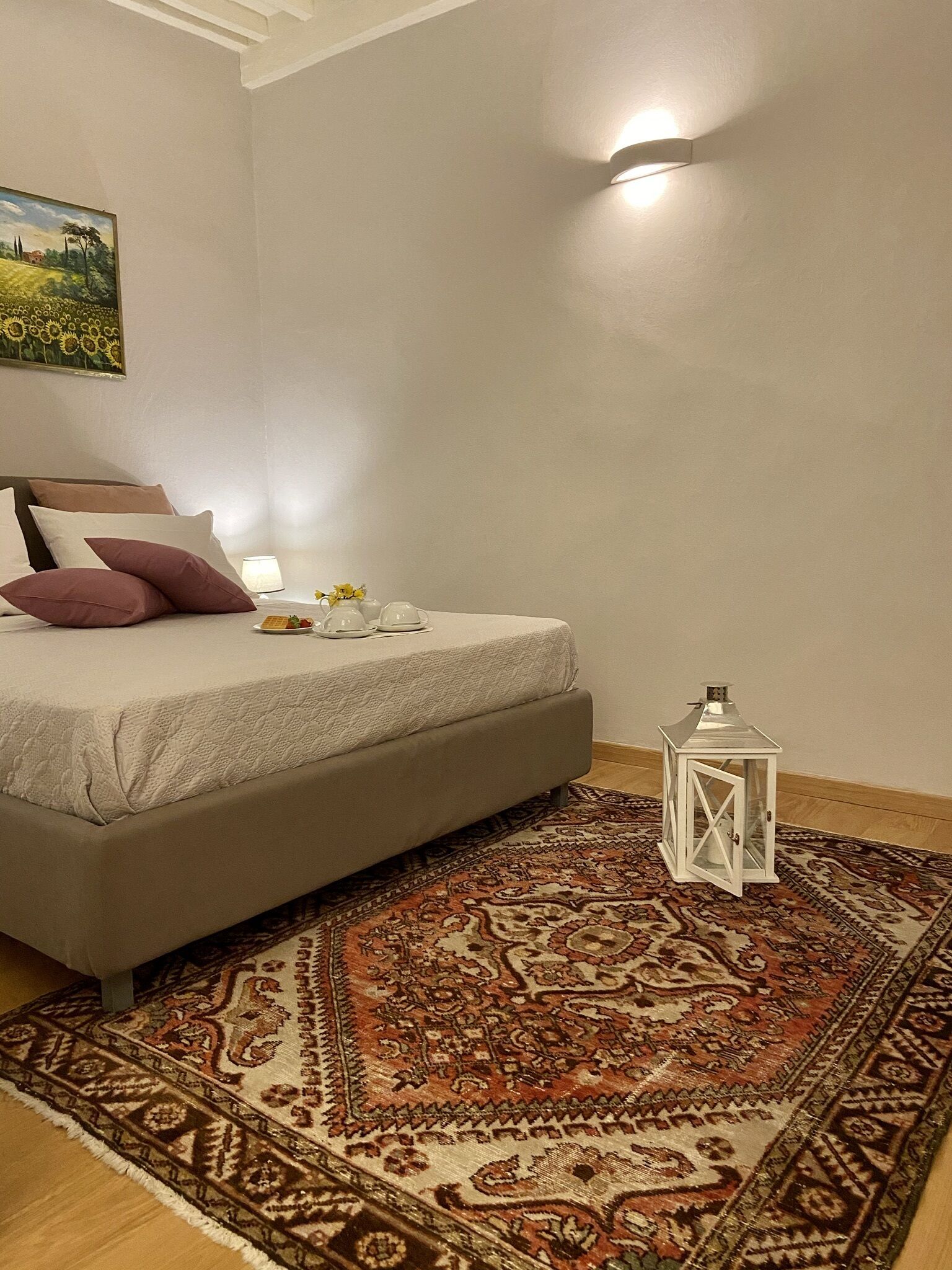 Ein Schlafzimmer mit einem Bett, einem gemusterten Teppich, einer Wandleuchte und einem Gemälde.
