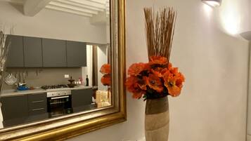 A modern kitchen with a large mirror, a vase with orange flowers, and a lit candle on the mantel.