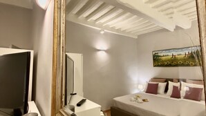A hotel room with a large mirror reflecting the ceiling, a bed with pillows, a bedside table with a lamp, and a TV on a stand. - sisters' home in the heart of Cortona (Cortona)
