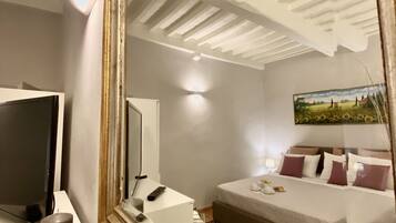 A hotel room with a large mirror reflecting the ceiling, a bed with pillows, a bedside table with a lamp, and a TV on a stand.