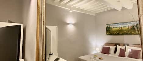 A hotel room with a large mirror reflecting the ceiling, a bed with pillows, a bedside table with a lamp, and a TV on a stand.